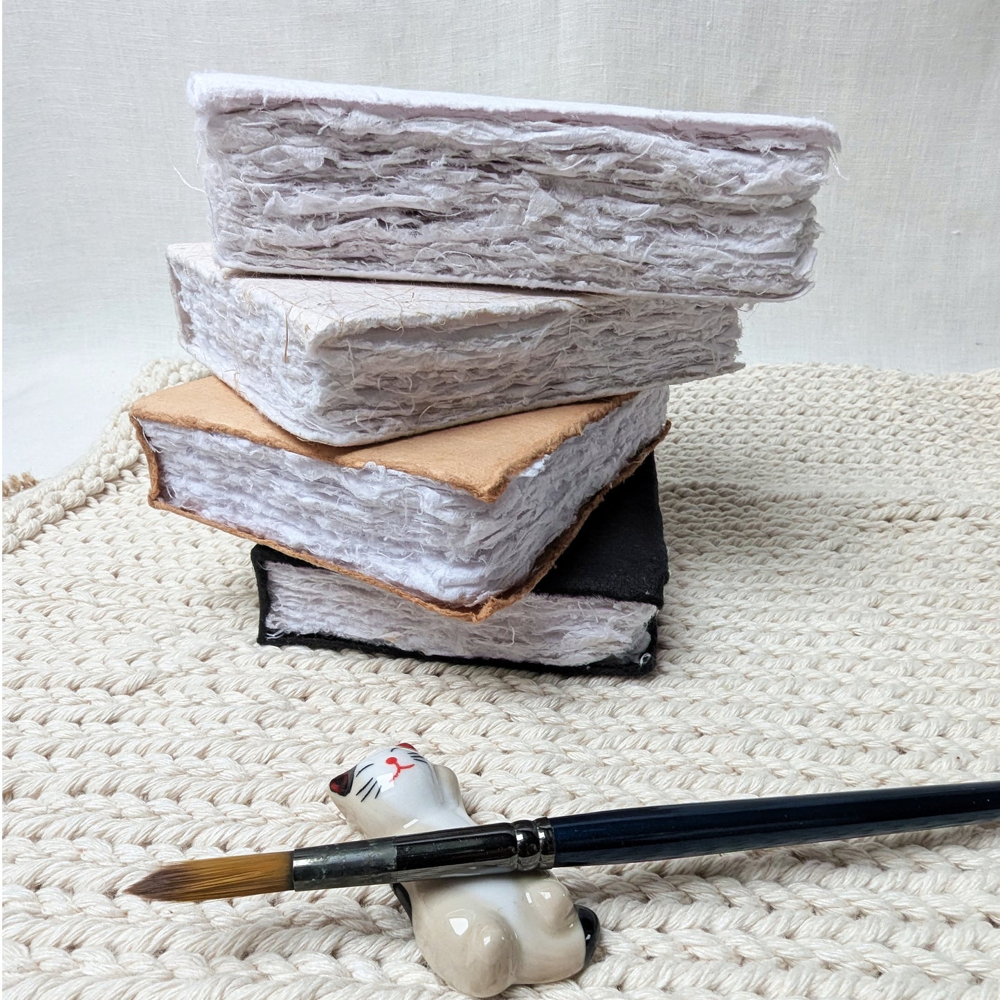 Stack of books with a small cat-shaped brush holder and paintbrush on a textured surface