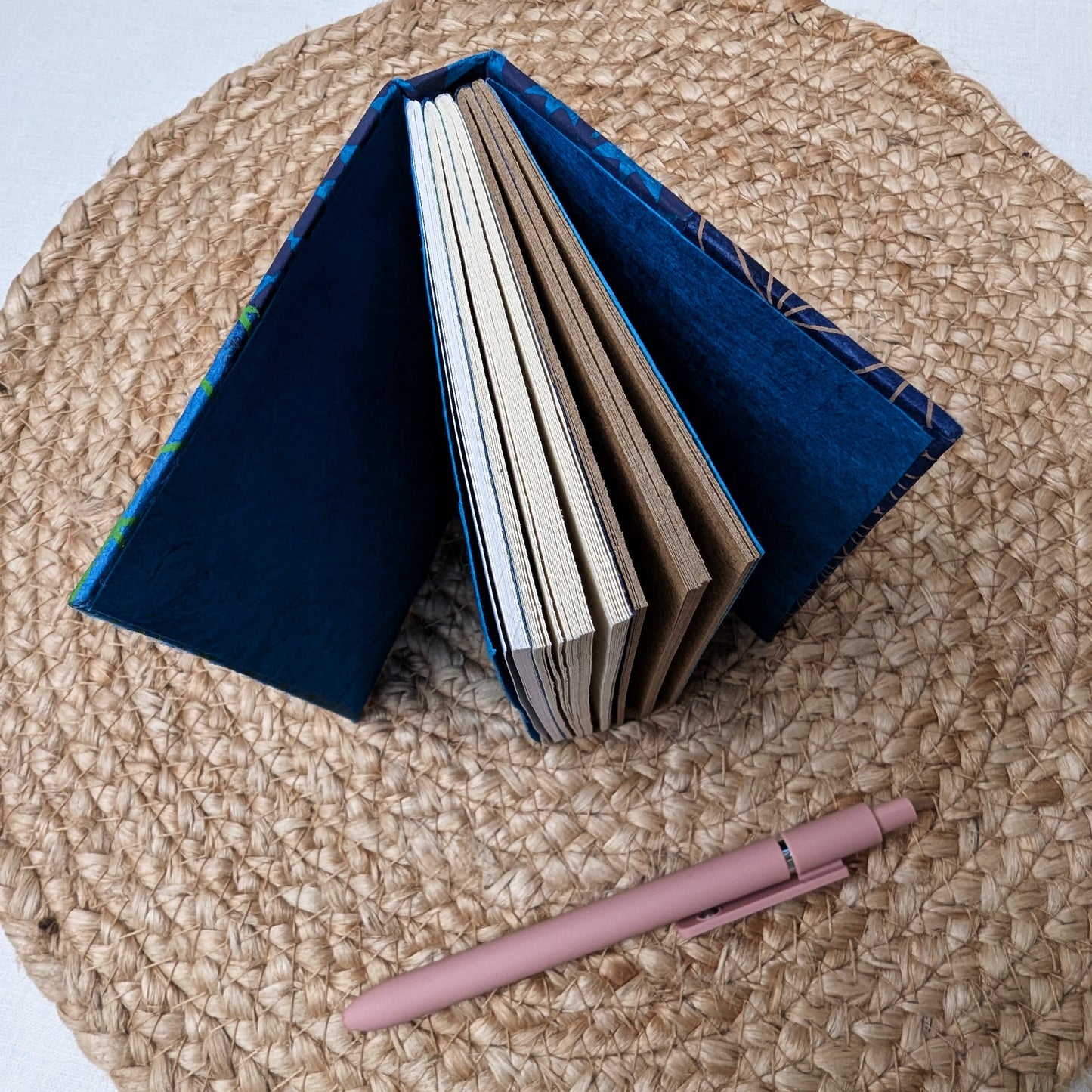 Open blue notebook with a pink pen on a woven surface