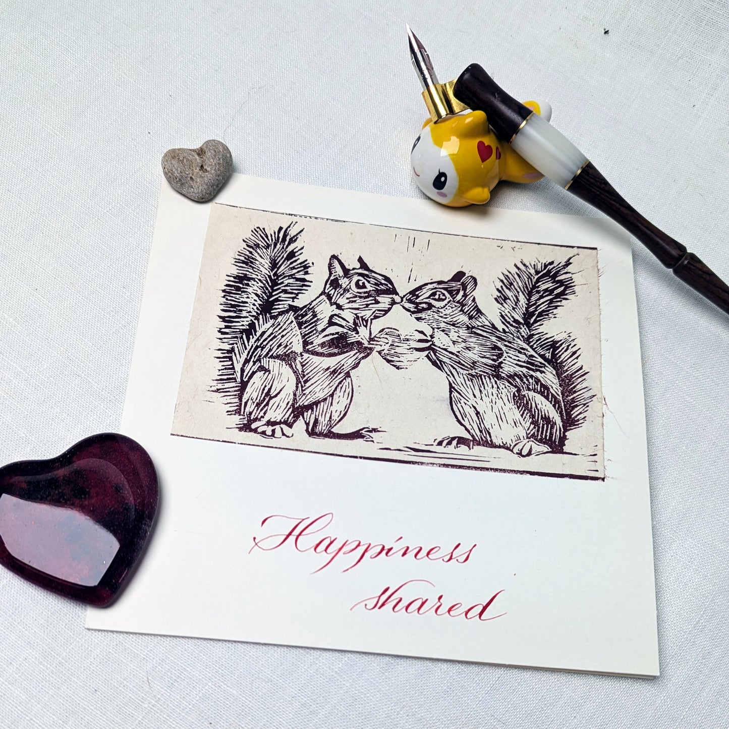 This handmade card features an original lino print of two squirrels leaning in close, caught in a moment that’s equal parts tenderness and cheek. It’s a light-hearted celebration of companionship, mutual joy, and the small, shared moments that make life brighter.

Each print is hand-pulled from a hand-carved lino block, giving the image depth, texture, and subtle variation. The accompanying text is written individually with a traditional dip pen and can be customised to suit your occasion.