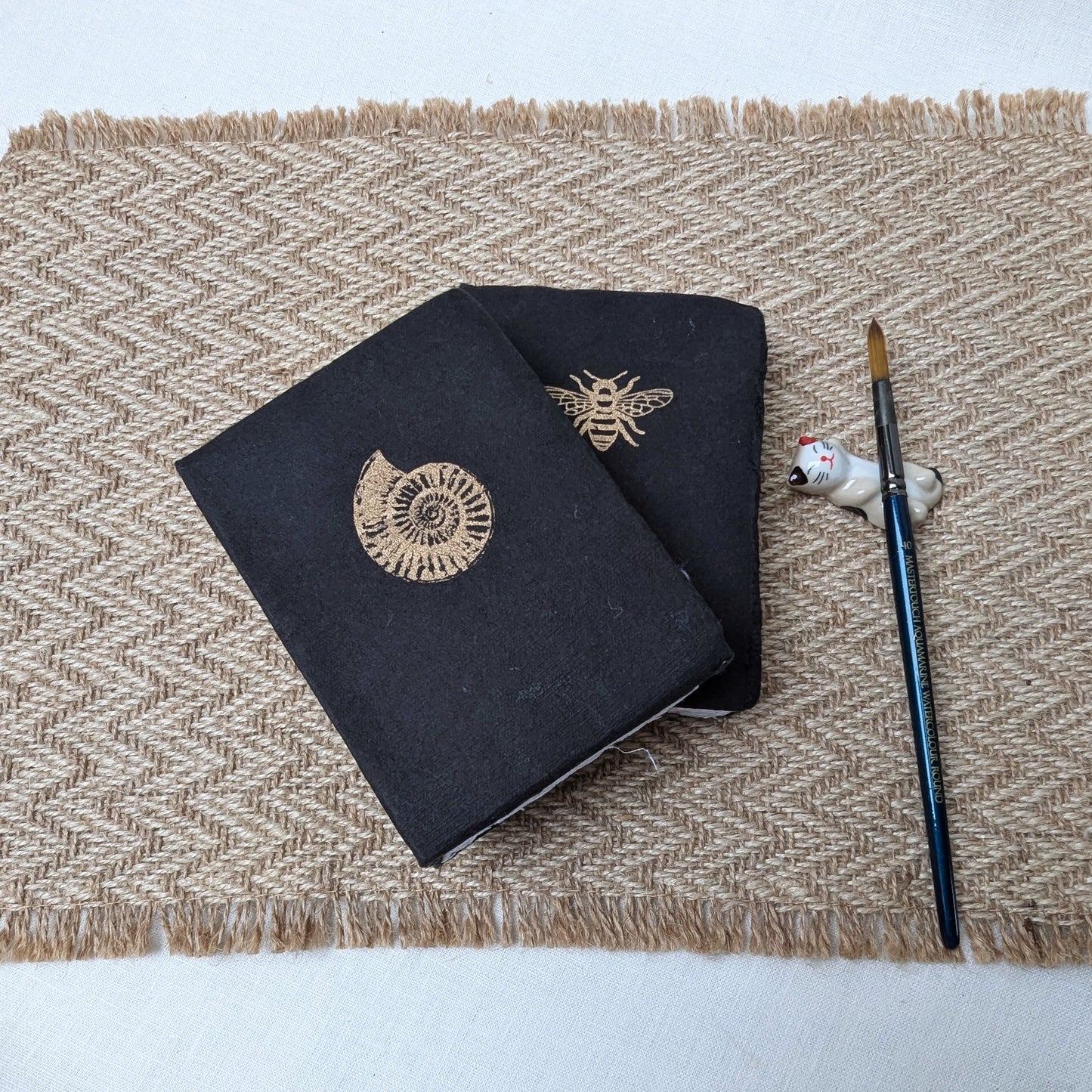Two black notebooks with embroidered designs on a textured surface