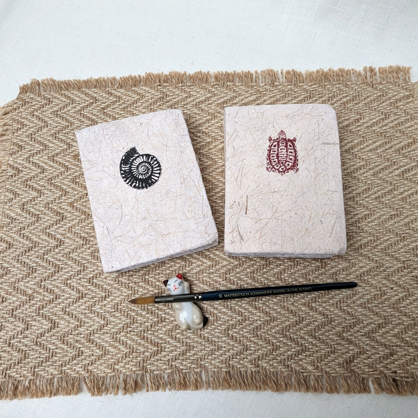 Two notebooks with decorative covers on a textured surface with a paintbrush and small ball.