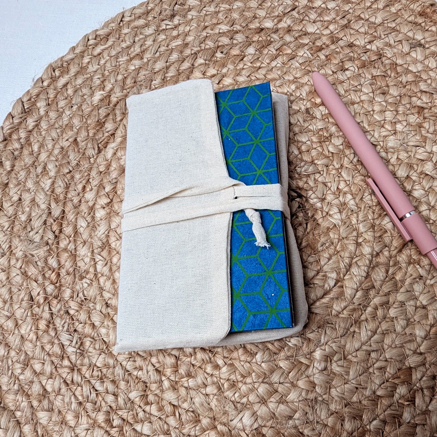 Notebook with a geometric cover, pink pen, and white case on a textured surface