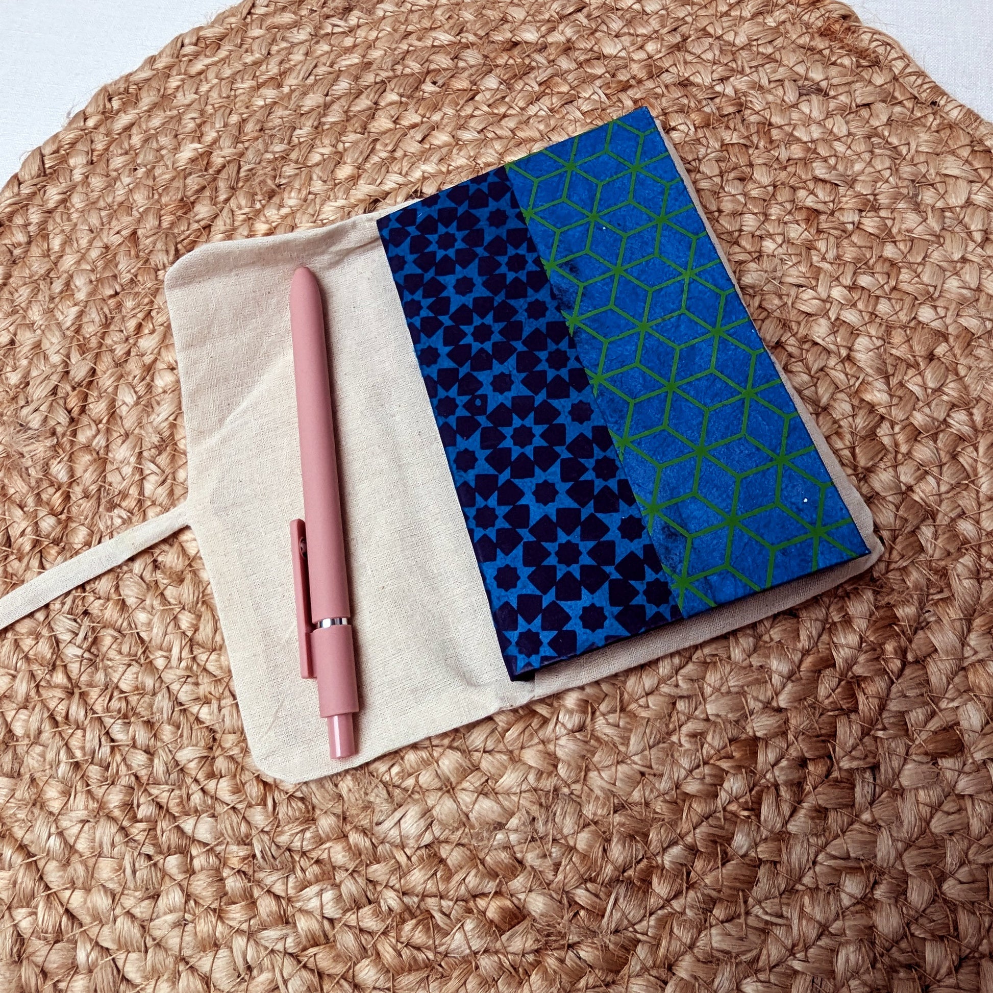 Notebook with blue geometric pattern and pink pen on woven surface
