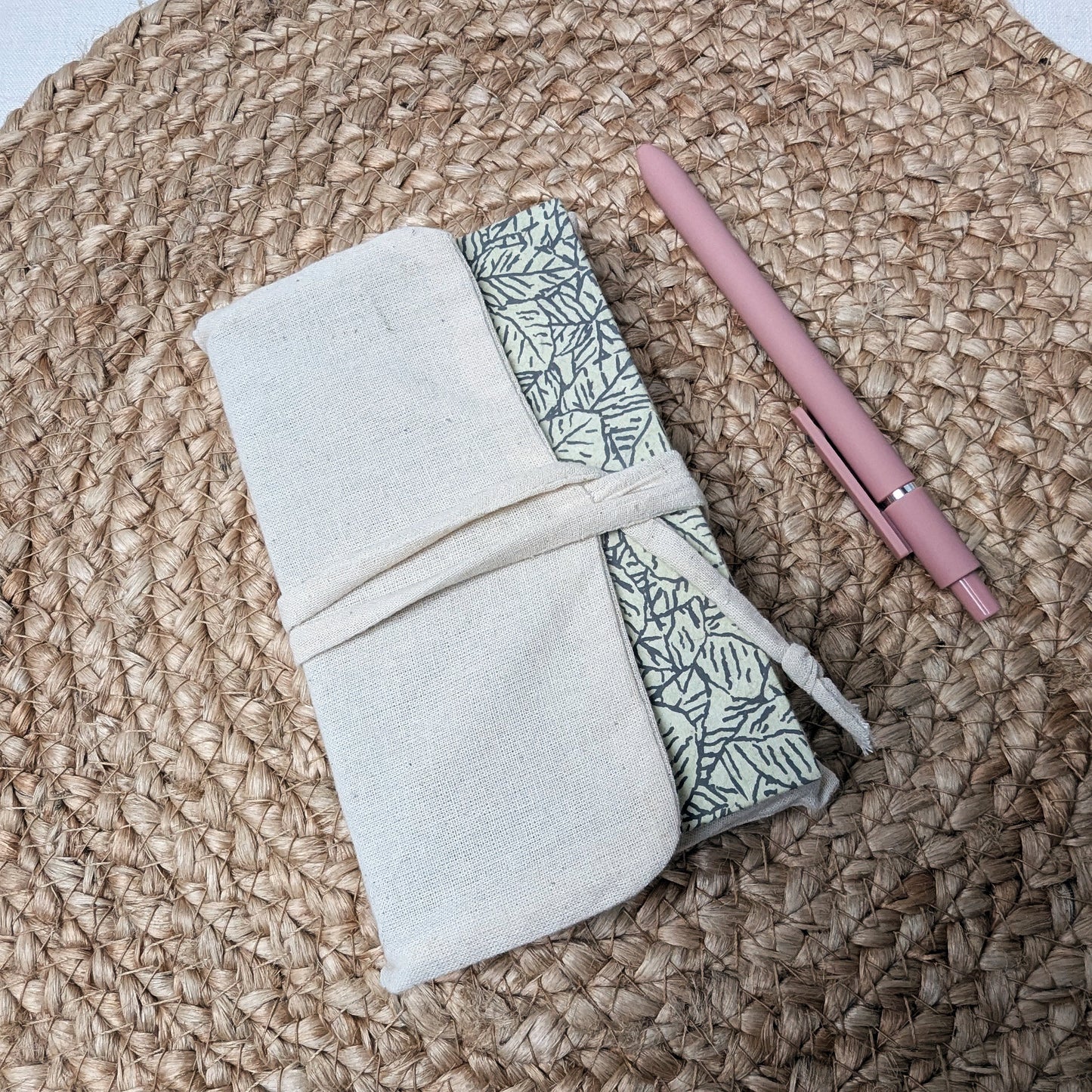 Folded fabric with leaf pattern and pink pen on a woven surface