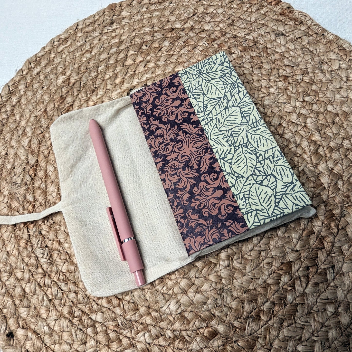 Two patterned notebooks and a pink pen on a textured surface