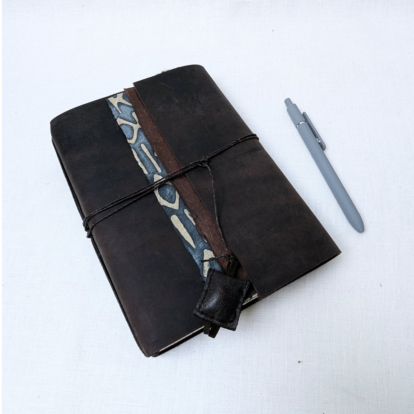 Brown leather notebook with patterned strap and gray pen on a white background