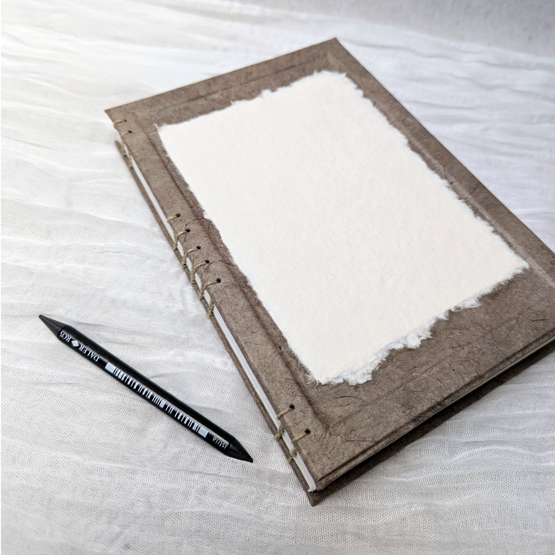 Brown art journal with white pages on a light gray surface, accompanied by a black pen.