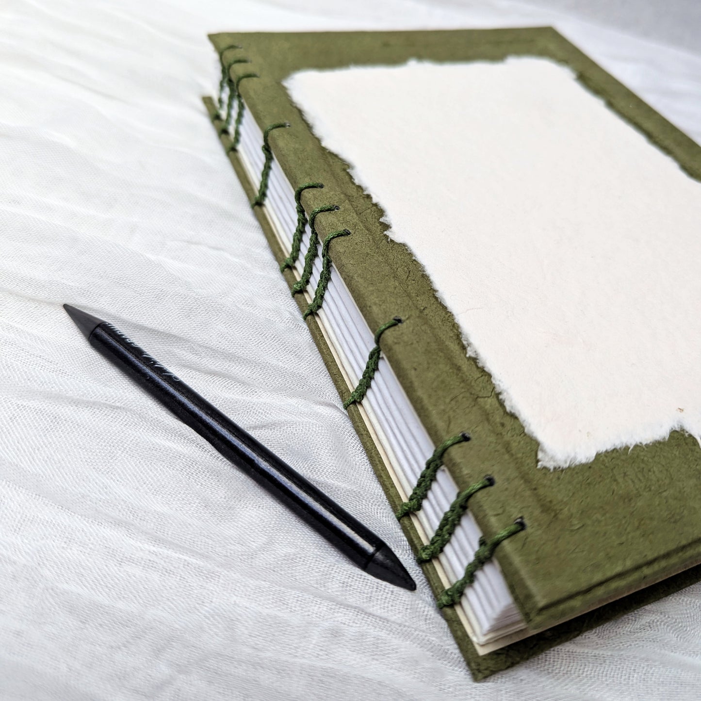 Green sketchbook with white pages and a pen on a white fabric background
