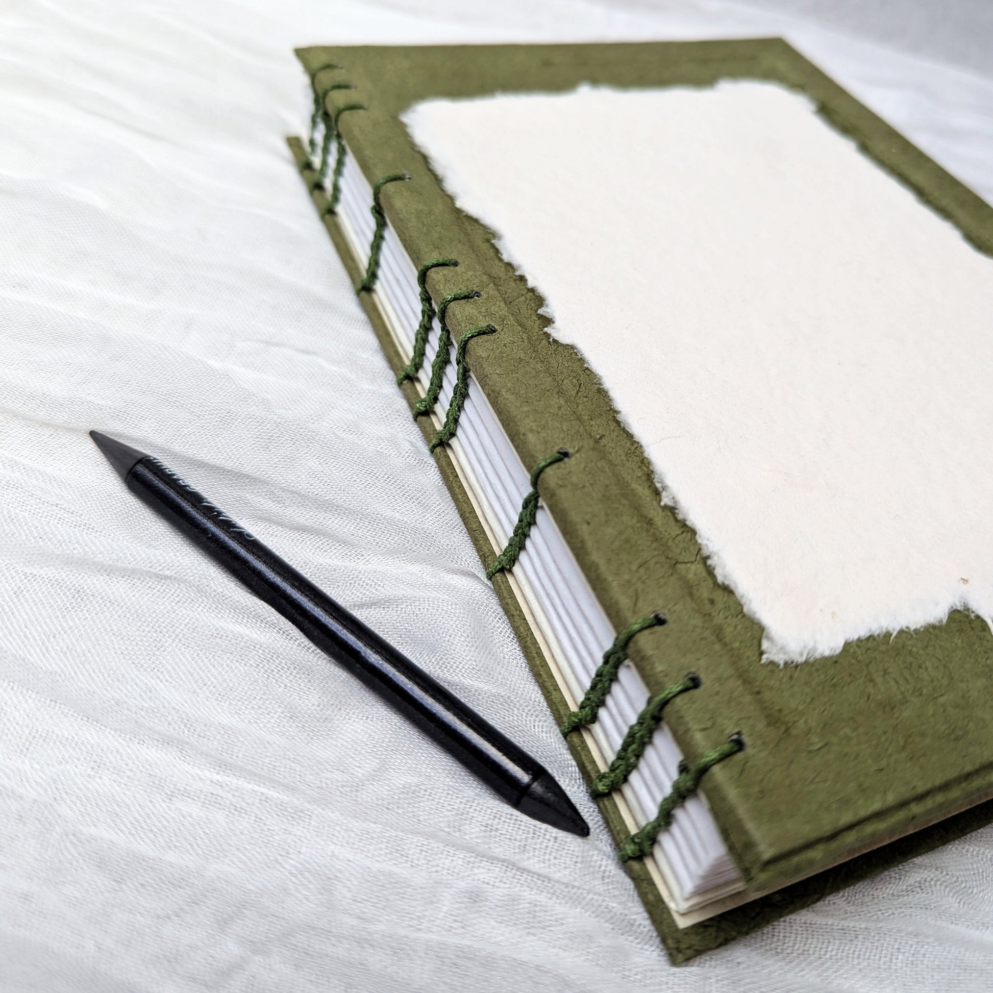 Green sketchbook with white pages and a pen on a white fabric background