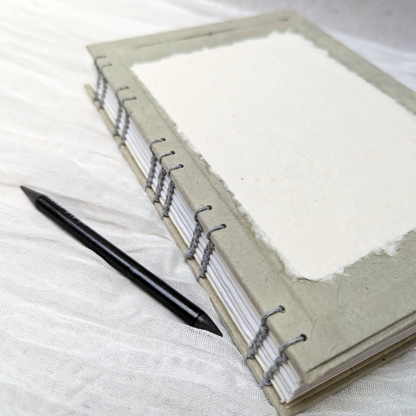 Grey drawing book with white pages and a black pen on a textured white surface