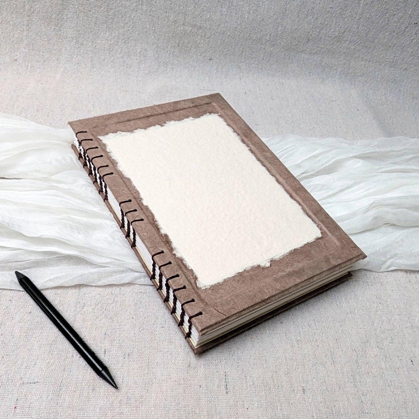 Brown coptic journal with thick white cartridge pages on a textured surface