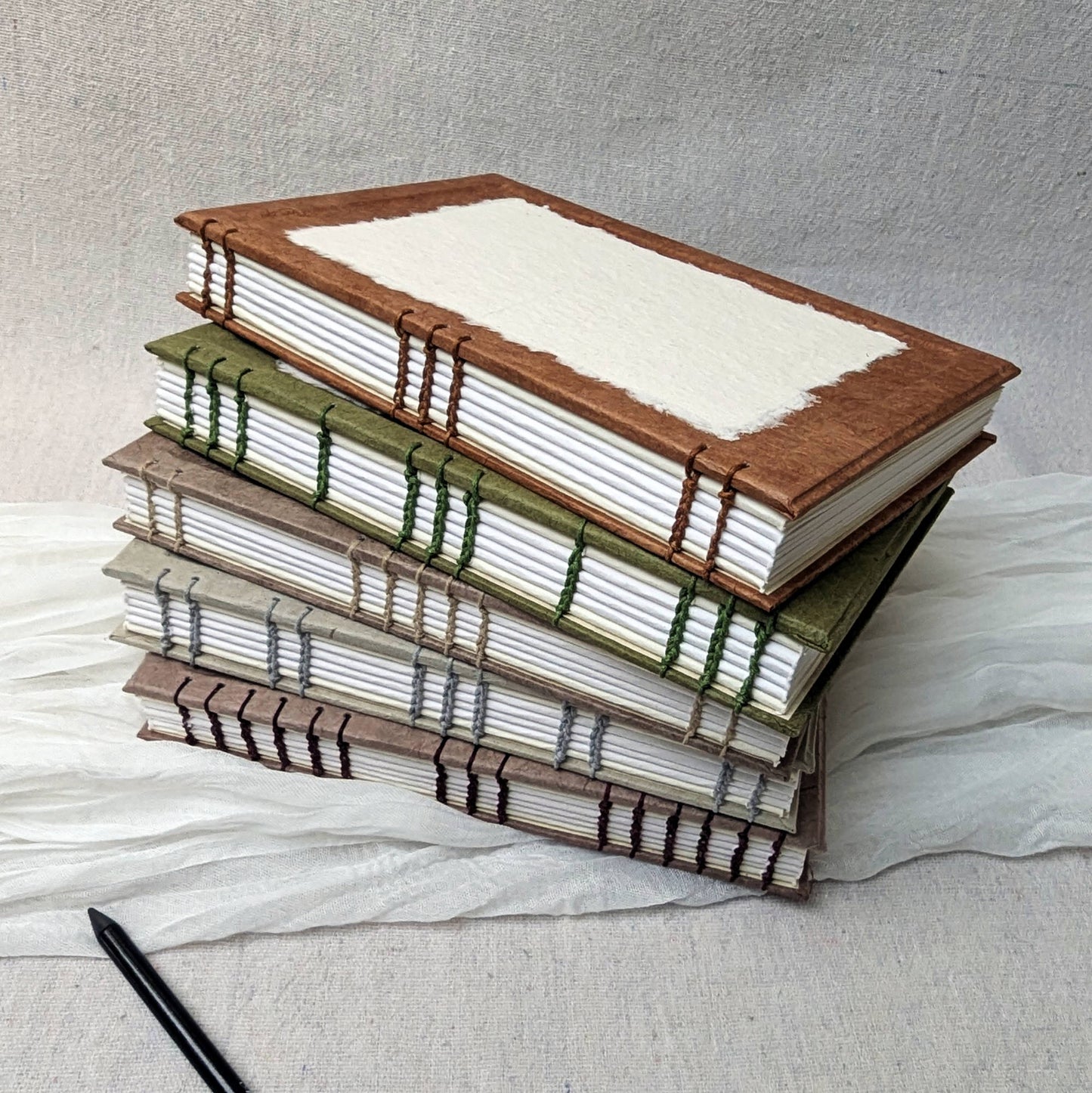 Stack of handmade A5 sketchbooks with coptic bindings with a customisable cover