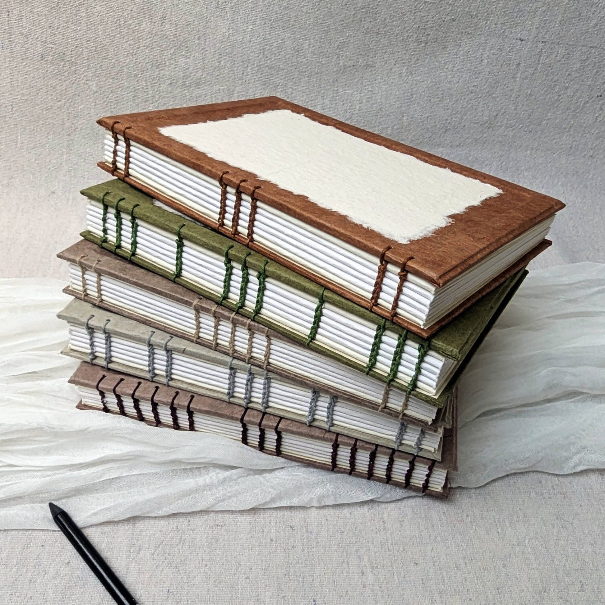 Stack of handmade A5 sketchbooks with coptic bindings with a customisable cover