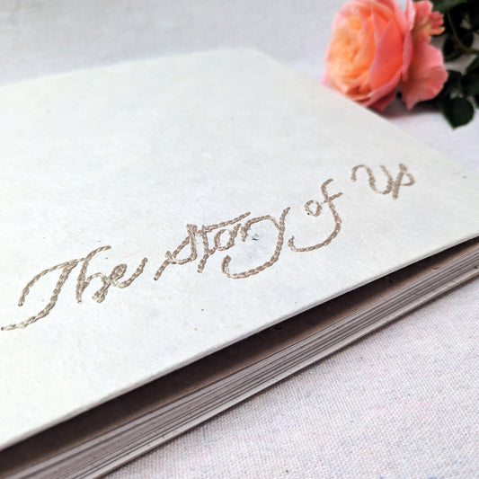 Close up embroidered photo album with “The Story of Us” on handmade white Lokta paper cover